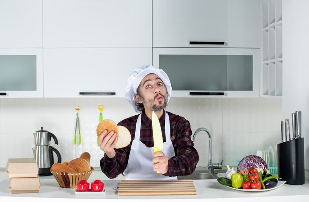 Vooraanzicht van een verbaasde mannelijke chef-kok met mes en brood in de keuken