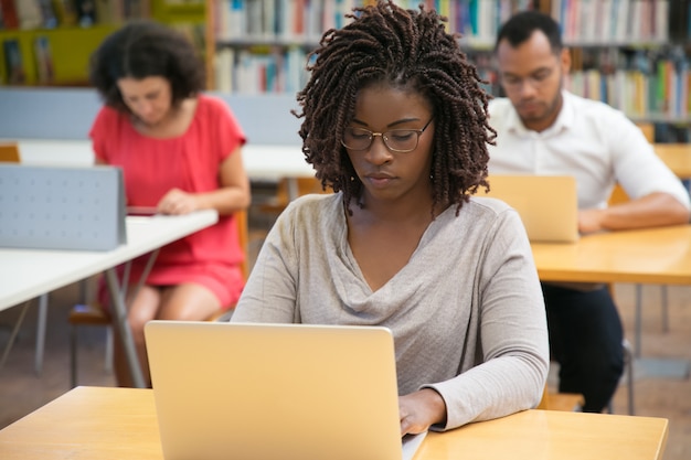 Vooraanzicht van geconcentreerde vrouw die met laptop bij bibliotheek werkt