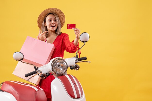 Vooraanzicht van gelukkige blonde vrouw in panama hoed op bromfiets met boodschappentassen en kaart