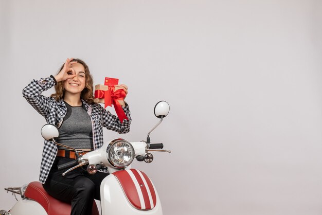 Vooraanzicht van gelukkige jonge vrouw die op de gift van de bromfietsholding handverrekijker op grijze muur maken