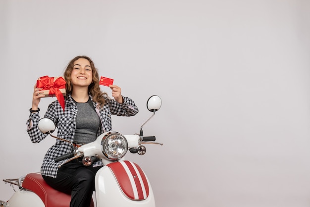 Vooraanzicht van gelukkige jonge vrouw op de kaart en de gift van de bromfietsholding