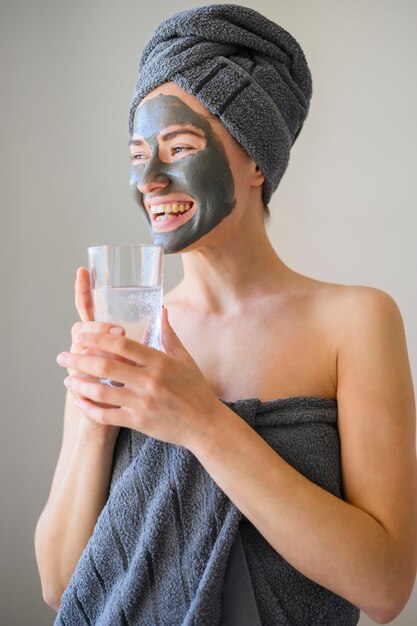 Vooraanzicht van gelukkige vrouw die gezichtsmasker draagt en glas water houdt