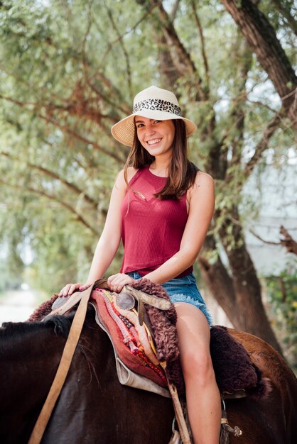 Vooraanzicht van glimlachende vrouw die een paard berijdt