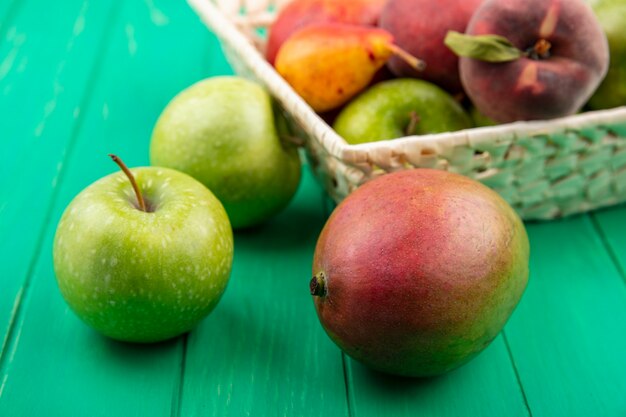 Vooraanzicht van groene appels met verschillende vruchten zoals peren perzik op een emmer op groene ondergrond