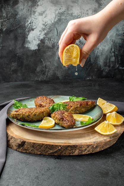 Vooraanzicht van hand knijpen limon op heerlijke schnitzels geserveerd met groenen op houten snijplank zwarte handdoek op donkere kleur achtergrond