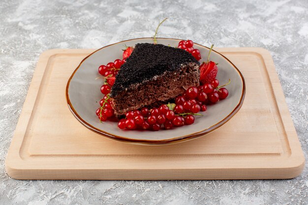 Vooraanzicht van heerlijke chocoladecake gesneden met chocoroom en verse rode Amerikaanse veenbessen op het houten bureau