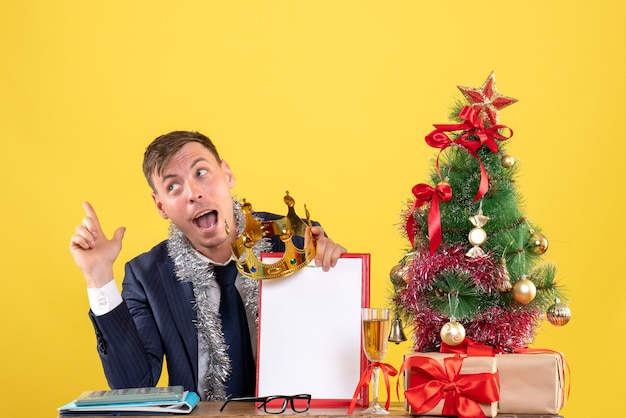 Vooraanzicht van het Klembord en de kroon van de bedrijfsmensenholding aan de tafel dichtbij de kerstboom en stelt op geel voor