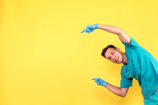 Vooraanzicht van het mannelijke arts stellen met blauwe handschoenen op gele muur