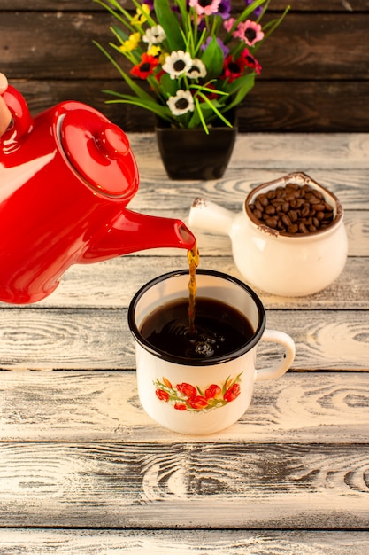 Vooraanzicht van hete kop gieten van rode ketel bruine koffie zaden en bloemen op het houten bureau