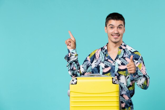 Vooraanzicht van jong mannetje dat voor reis met zijn gele zak op de lichtblauwe muur voorbereidingen treft