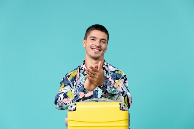 Vooraanzicht van jong mannetje dat voor vakantie met zak klappen voorbereidt en op blauwe muur glimlacht