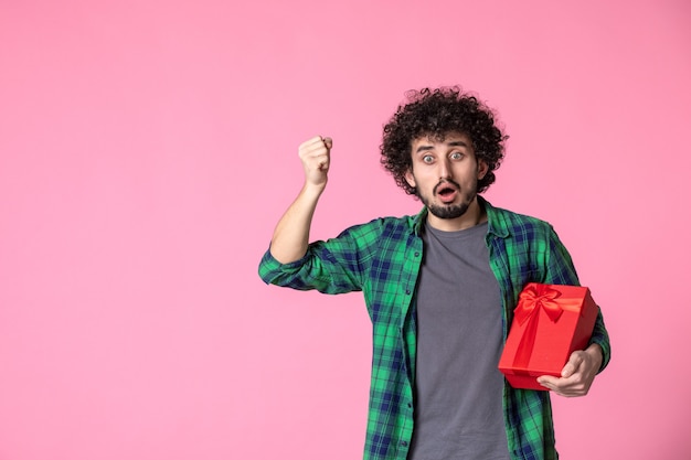 Vooraanzicht van jong mannetje met rood pakket op lichtroze muur