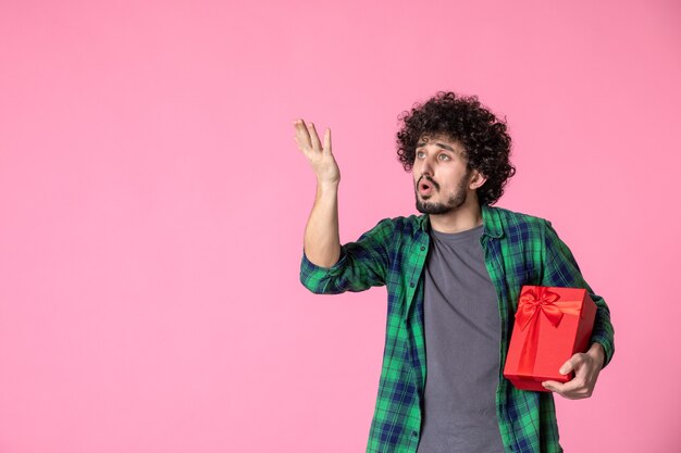 Vooraanzicht van jong mannetje met rood pakket op lichtroze muur