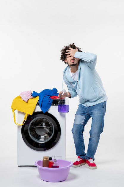 Vooraanzicht van jong mannetje met wasmachine die vloeibaar poeder op witte muur houdt