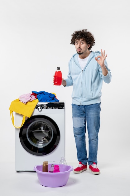 Vooraanzicht van jong mannetje met wasmachine die vloeibaar poeder op witte muur houdt