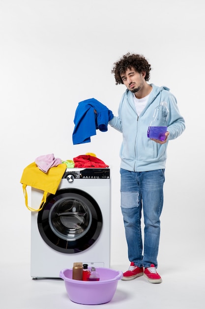 Vooraanzicht van jong mannetje met wasmachine die vloeibaar poeder op witte muur houdt