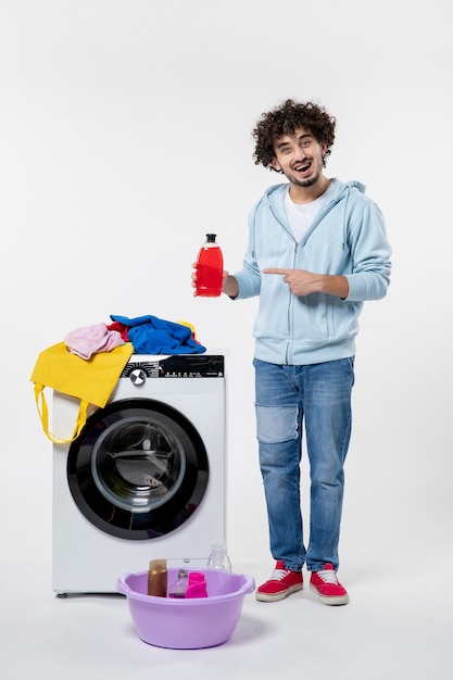 Vooraanzicht van jong mannetje met wasmachine die vloeibaar poeder op witte muur houdt