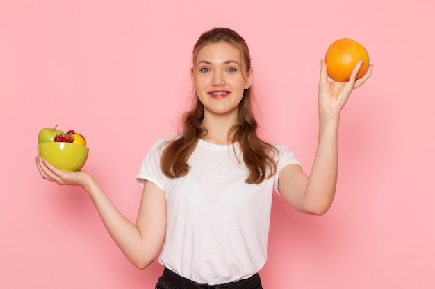 Vooraanzicht van jong wijfje in de witte plaat van de t-shirtholding met vers fruit het glimlachen