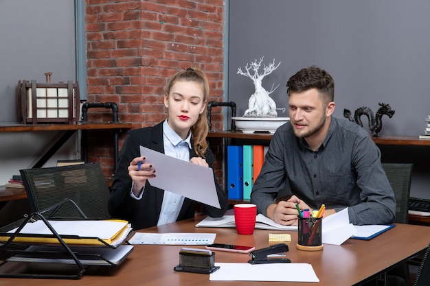 Vooraanzicht van jonge hardwerkende bedienden die één probleem bespreken in de documenten op kantoor