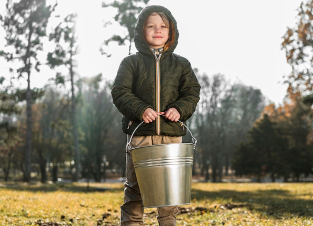 Gratis foto vooraanzicht van jonge jongen die buitenshuis emmer houdt