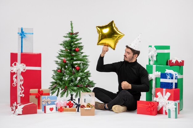 Vooraanzicht van jonge man die rondhangen cadeautjes en gouden stercijfer op witte muur houdt