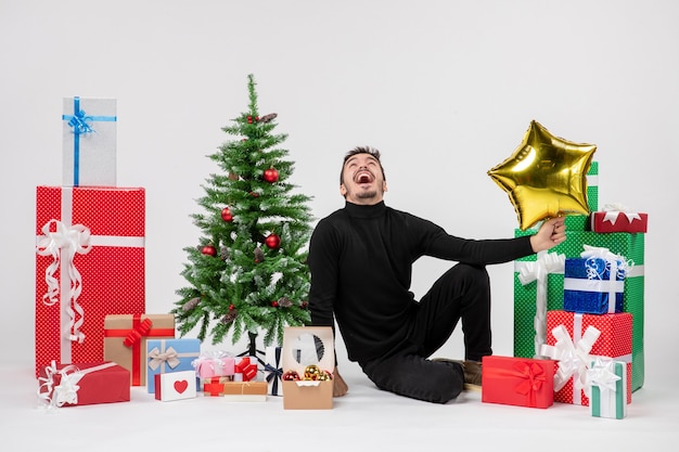 Vooraanzicht van jonge man die rondhangen cadeautjes en gouden stercijfer op witte muur houdt