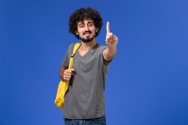 Vooraanzicht van jonge man in grijs t-shirt gele rugzak dragen op de blauwe muur