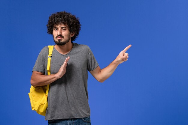 Vooraanzicht van jonge man in grijs t-shirt met gele rugzak die net op de blauwe muur poseren