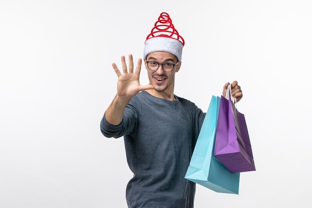 Vooraanzicht van jonge man met cadeautjes na het winkelen op witte muur