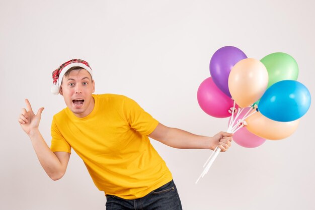 Vooraanzicht van jonge man met kleurrijke ballonnen op witte muur