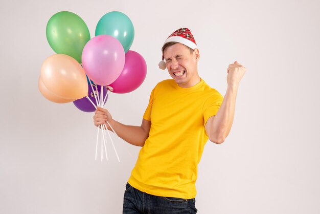 Vooraanzicht van jonge man met kleurrijke ballonnen op witte muur