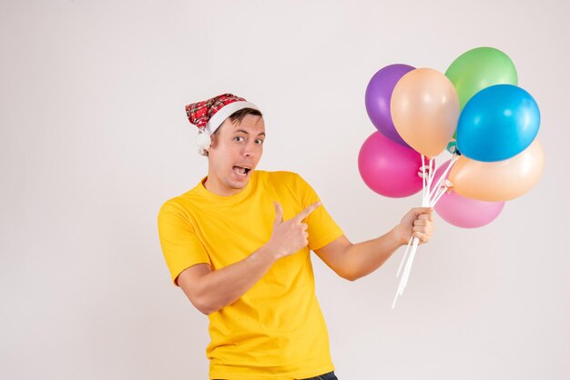 Vooraanzicht van jonge man met kleurrijke ballonnen op witte muur