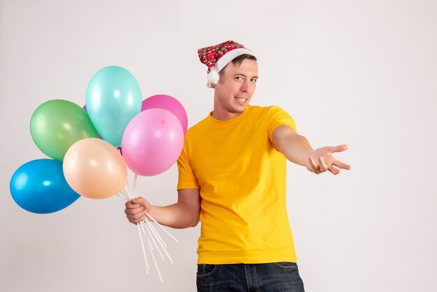 Vooraanzicht van jonge man met kleurrijke ballonnen op witte muur