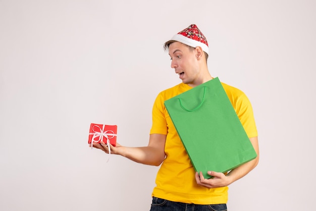 Vooraanzicht van jonge man met pakket en klein cadeautje op witte muur