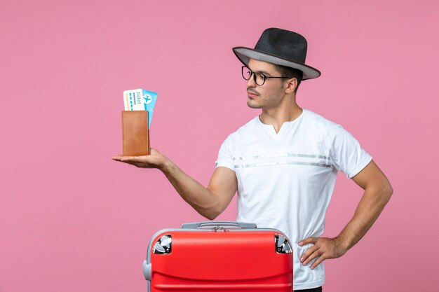 Vooraanzicht van jonge man met vakantiekaartjes op roze muur