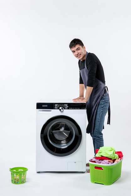 Vooraanzicht van jonge man met vuile kleren en wasmachine op witte muur