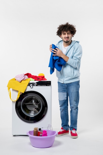 Vooraanzicht van jonge man met wasmachine en vuile kleren op witte muur