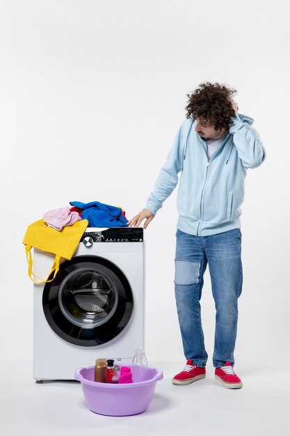 Gratis foto vooraanzicht van jonge man met wasmachine en vuile kleren op witte muur