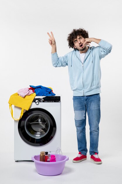 Vooraanzicht van jonge man met wasmachine en vuile kleren op witte muur