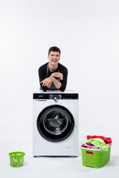 Vooraanzicht van jonge man met wasmachine en vuile kleren op witte muur