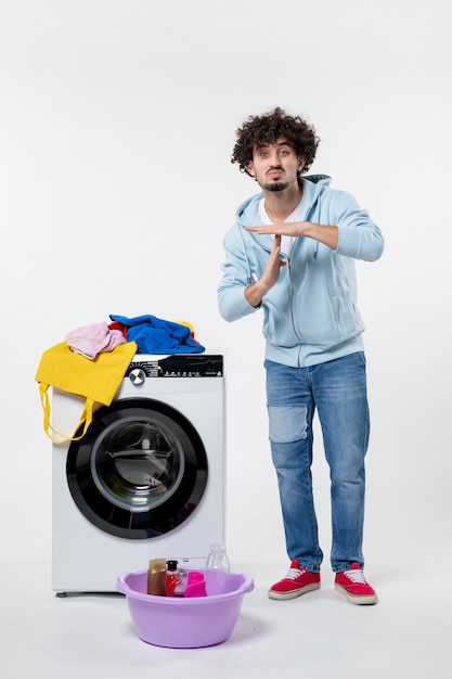 Vooraanzicht van jonge man met wasmachine en vuile kleren op witte muur