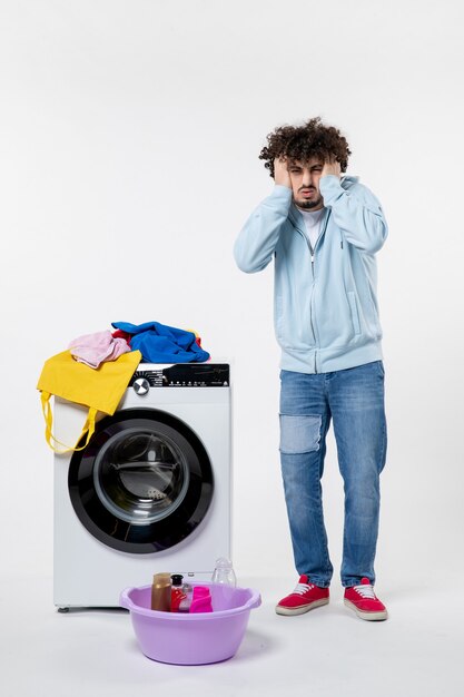 Gratis foto vooraanzicht van jonge man met wasmachine en vuile kleren op witte muur