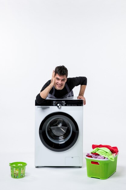 Vooraanzicht van jonge man met wasmachine en vuile kleren op witte muur