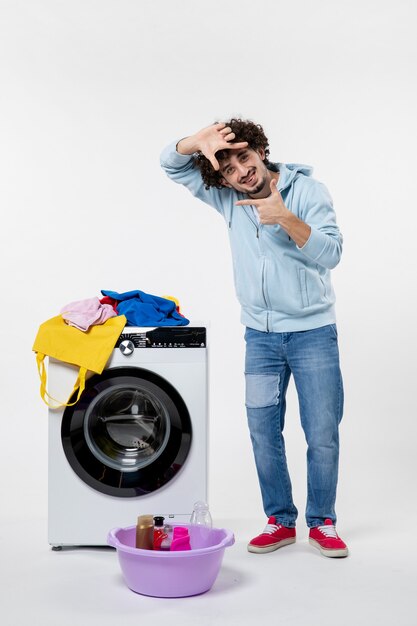 Vooraanzicht van jonge man met wasmachine en vuile kleren op witte muur