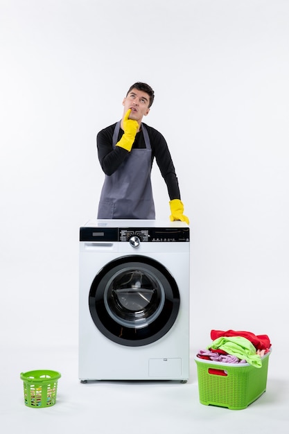 Vooraanzicht van jonge man met wasmachine en vuile kleren op witte muur