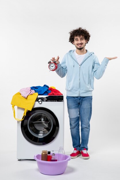 Vooraanzicht van jonge man met wasmachine met klokken op witte muur