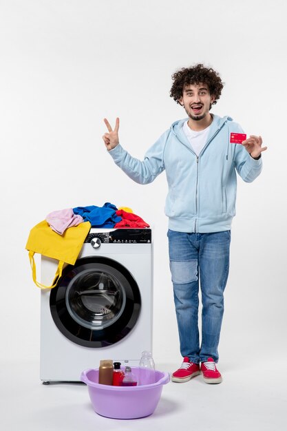 Vooraanzicht van jonge man met wasmachine met rode bankkaart op witte muur