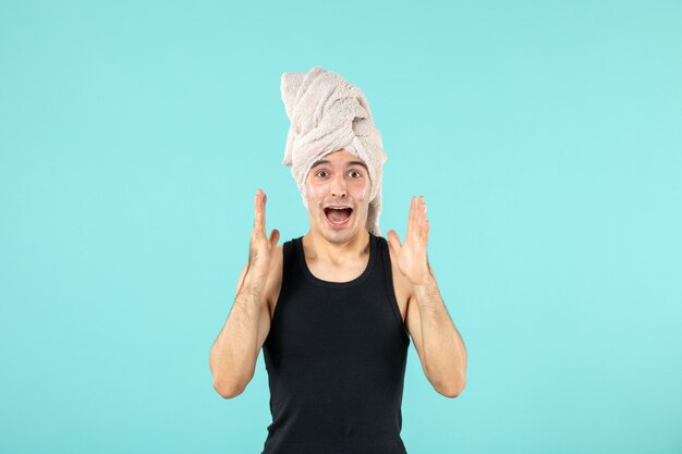 vooraanzicht van jonge man na het douchen die crème op zijn gezicht op blauwe muur aanbrengt