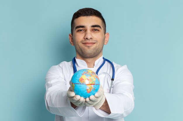 Vooraanzicht van jonge mannelijke arts in wit kostuum met de blauwe bol van de stethoscoopholding