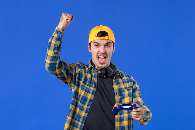 Vooraanzicht van jonge opgewonden man met gamepad die videogame speelt op blauwe muur